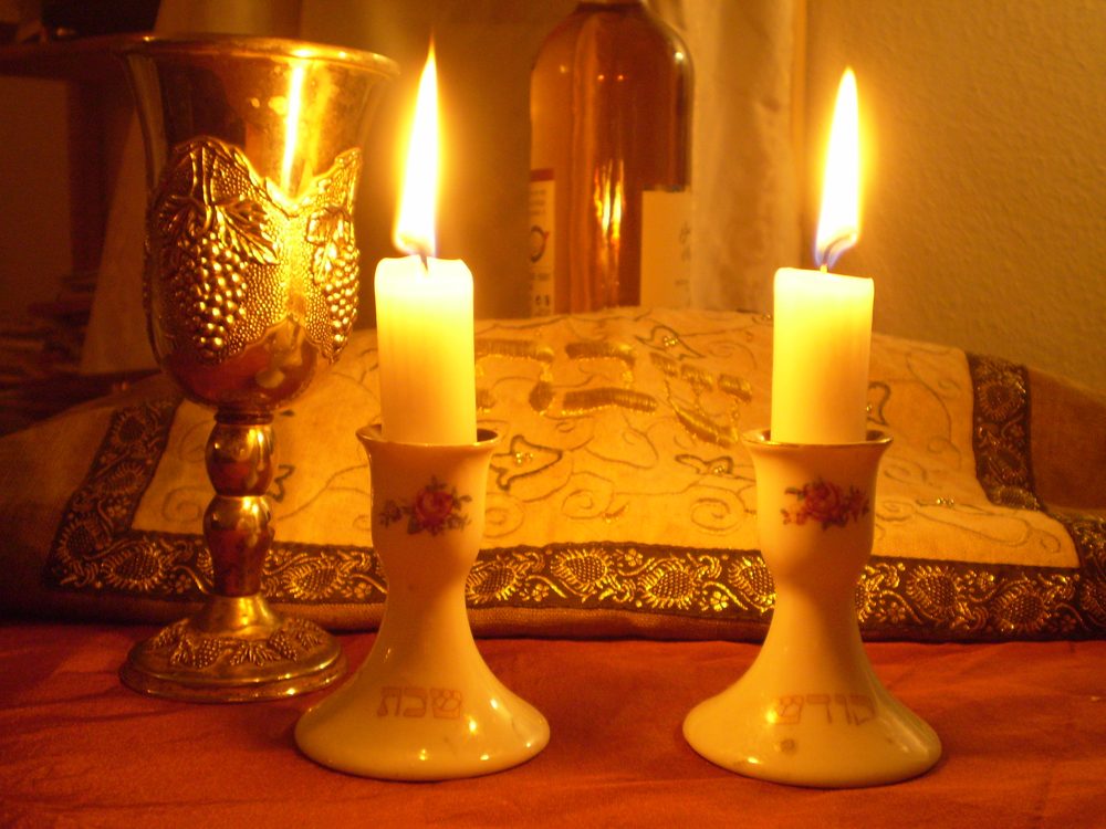 Lit Shabbat candles beside a kiddush cup and covered challah
