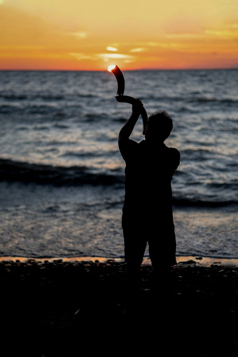 Silhouette of a person sounding the shofar at sunset